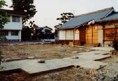 手前の雨水を受ける溝によって、本堂の屋根の向拝のあった位置を、うかがい知ることができる。右手は仮本堂として残った庫裡。